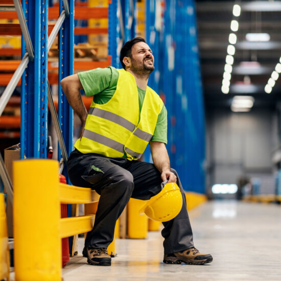 A storage worker in pain having back pain and massage the painful place.